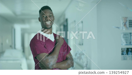 Standing doctor wearing burgundy scrubs in hospital corridor with gurney, digital overlays Standing doctor wearing burgundy scrubs in hospital corridor with gurney, digital overlays 139254927