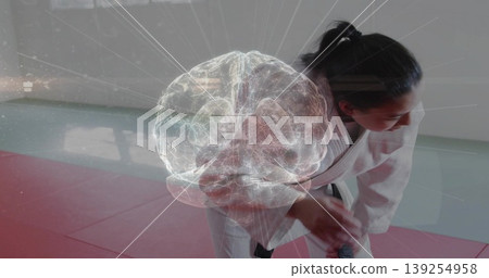 Bending martial artist in white gi adjusting black belt knot on red mats, with brain hologram 139254958