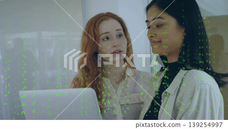 Two female colleagues collaborating at modern office desk, with laptop streaming green binary code Two female colleagues collaborating at modern office desk, with laptop streaming green binary code 139254997