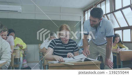 Reading teenage student holding pen at desk in classroom, with instructor pointing at textbook Reading teenage student holding pen at desk in classroom, with instructor pointing at textbook 139255044