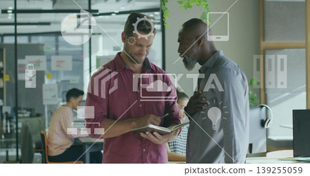 Discussing colleagues in maroon and grey shirts taking notes in office, with notebook and monitor Discussing colleagues in maroon and grey shirts taking notes in office, with notebook and monitor 139255059