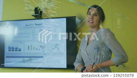 Presenting consultant in dress pointing to glass board in meeting, with monitor, stylus, copy space 139255079
