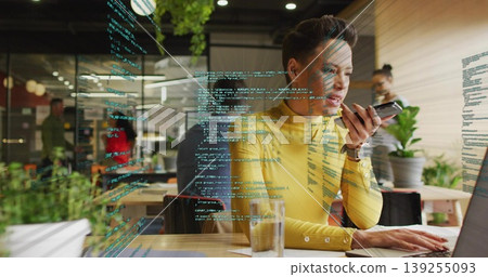 Typing woman in yellow sweater talking into smartphone at office with code on glass partition Typing woman in yellow sweater talking into smartphone at office with code on glass partition 139255093