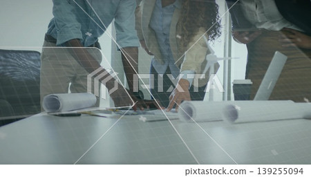 Leaning three professionals reviewing blueprints and tablet in meeting room, with coffee cup Leaning three professionals reviewing blueprints and tablet in meeting room, with coffee cup 139255094