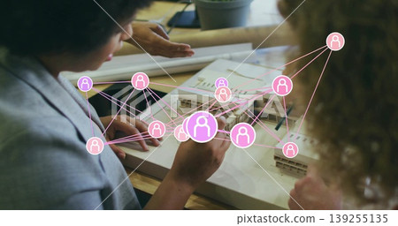 Group of four architects examining scale model and plans in studio, with pink network icons, tablet Group of four architects examining scale model and plans in studio, with pink network icons, tablet 139255135