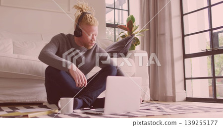 Typing male wearing gray sweater and headphones on patterned rug in living room, with laptop, mug Typing male wearing gray sweater and headphones on patterned rug in living room, with laptop, mug 139255177