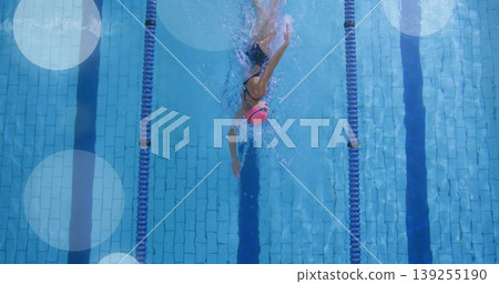 Gliding female swimmer stroking through tiled pool lane with cap goggles swimsuit and divider ropes Gliding female swimmer stroking through tiled pool lane with cap goggles swimsuit and divider ropes 139255190