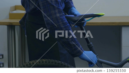 Adjusting mechanic wearing gloves positioning saddle height in workshop with mountain bike frame 139255330