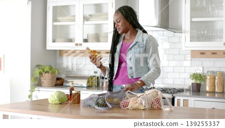 Inspecting woman wearing denim jacket holding oil bottle at kitchen island, with produce bags 139255337