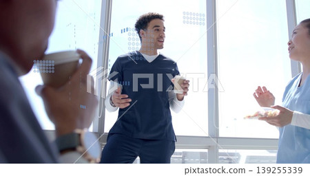 Leaning professional wearing scrubs holding coffee cups in break room by windows, with snack plate Leaning professional wearing scrubs holding coffee cups in break room by windows, with snack plate 139255339