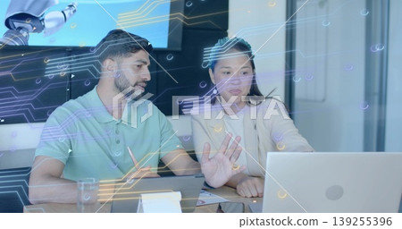 Tech professionals analyzing data using laptop in office, with stylus and robotic arm Tech professionals analyzing data using laptop in office, with stylus and robotic arm 139255396