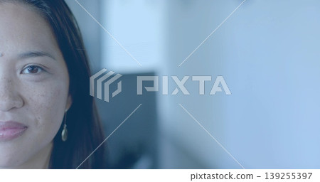 Gazing Asian woman focusing forward in office, with gold earring, blurred monitor, copy space 139255397