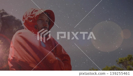 Standing man wearing red hooded parka gazing across rocky ridge with evergreen branches, copy space Standing man wearing red hooded parka gazing across rocky ridge with evergreen branches, copy space 139255461