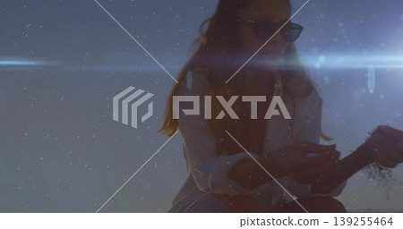 Examining dried plant, woman in white shirt, sunglasses under lens-flare streak on dune, copy space Examining dried plant, woman in white shirt, sunglasses under lens-flare streak on dune, copy space 139255464