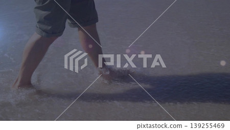 Man wading through shallow water on wet sand at beach shoreline, with rolled-up shorts, copy space Man wading through shallow water on wet sand at beach shoreline, with rolled-up shorts, copy space 139255469