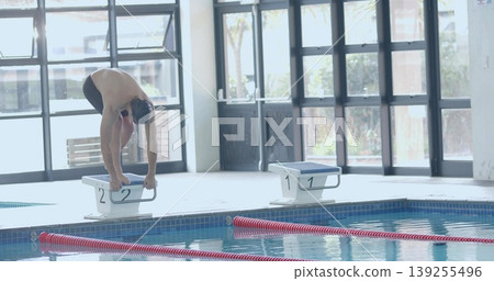 Bending shirtless male swimmer gripping block 2 preparing to dive at pool with goggles, copy space 139255496