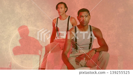 Sitting two men wearing grey tops, beige pants and suspenders on studio stools showing wristwatch 139255525