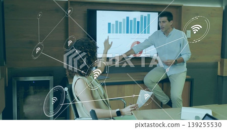Holding smartphone, casually dressed colleagues discussing chart data in boardroom with display 139255530