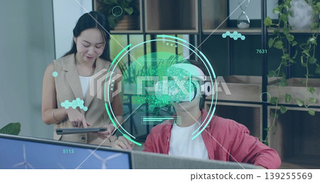 Pointing woman holding tablet and guiding man wearing red jacket, VR headset at office desk Pointing woman holding tablet and guiding man wearing red jacket, VR headset at office desk 139255569