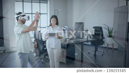 Colleagues manipulating interface in office near grid window, wearing VR headset and using tablet Colleagues manipulating interface in office near grid window, wearing VR headset and using tablet 139255585