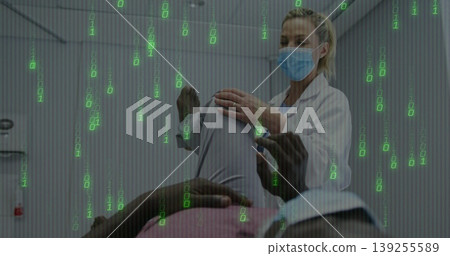 Masked doctor supporting patient's raised leg while assessing knee in clinic, with table and lights 139255589