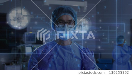 Standing Chinese surgeon performing surgical prep in operating room, with lights and monitors Standing Chinese surgeon performing surgical prep in operating room, with lights and monitors 139255592