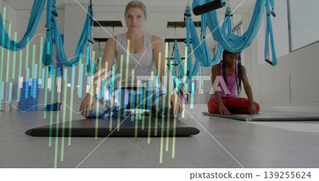 Kneeling woman wearing activewear analyzing biometric data on mat in studio with aerial hammocks 139255624
