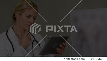 Female doctor wearing lab coat studying tablet in clinic with stethoscope and chart, copy space Female doctor wearing lab coat studying tablet in clinic with stethoscope and chart, copy space 139255670