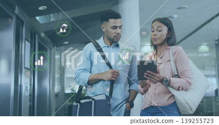Walking colleagues explaining tablet data in modern office corridor, carrying bags and smartwatches 139255723