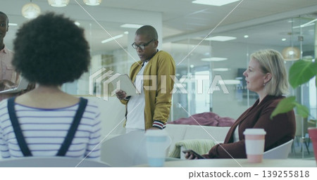 Reading from tablet African American man wearing mustard cardigan in office lounge, with papers Reading from tablet African American man wearing mustard cardigan in office lounge, with papers 139255818