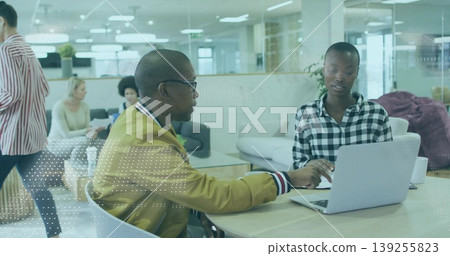 Collaborating bomber-jacketed man and checkered shirt woman working on laptop in office lounge 139255823