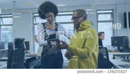 Analyzing tablet with stylus, man in mustard hoodie and woman in overalls in office with monitors 139255827