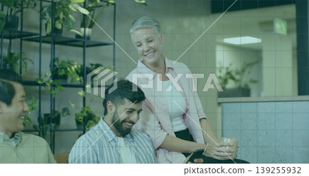 Smiling coworkers leaning around tablet on bench in office lounge, with mug and shelving unit 139255932