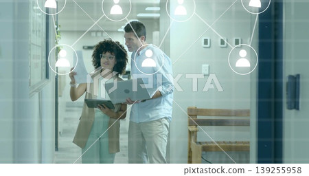 Reviewing colleagues wearing business attire examining board in office corridor, with laptop paper 139255958