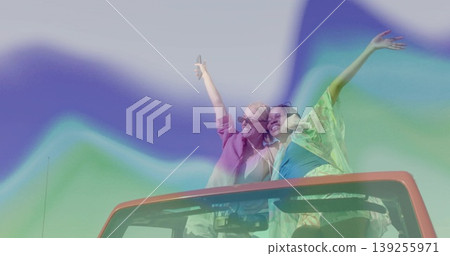 Standing friends wearing shades raising arms out of red convertible roof snapping selfie with phone Standing friends wearing shades raising arms out of red convertible roof snapping selfie with phone 139255971
