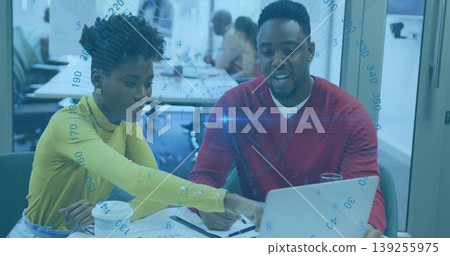 Coworkers in yellow top and red sweater reviewing laptop data at open-plan office, with coffee cup Coworkers in yellow top and red sweater reviewing laptop data at open-plan office, with coffee cup 139255975