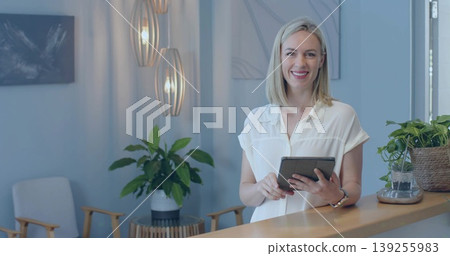 Holding tablet, receptionist typing notes behind reception desk, pendants and plants, copy space Holding tablet, receptionist typing notes behind reception desk, pendants and plants, copy space 139255983
