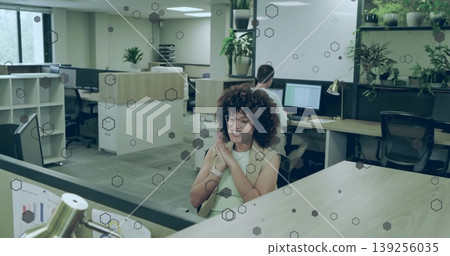 Smiling African American woman typing on keyboard in office showing hexagon partition and monitors Smiling African American woman typing on keyboard in office showing hexagon partition and monitors 139256035