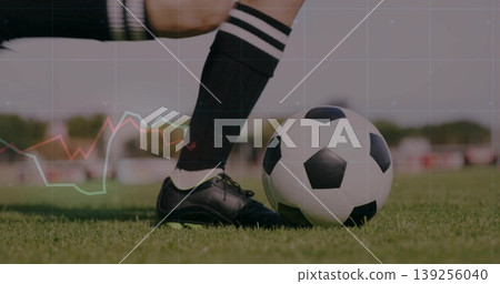 Pressing female athlete's black soccer cleat onto ball on grass pitch, with striped athletic sock 139256040