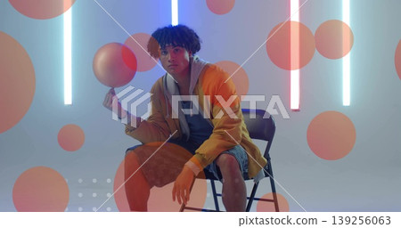 Spinning man in yellow jacket balancing sphere on finger in studio with neon lights, orange circles Spinning man in yellow jacket balancing sphere on finger in studio with neon lights, orange circles 139256063
