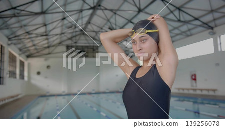 Adjusting swimmer fitting swimsuit, cap and yellow goggles at pool, with lane dividers, copy space Adjusting swimmer fitting swimsuit, cap and yellow goggles at pool, with lane dividers, copy space 139256078