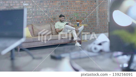 Sitting Indian man holding notebook and pen on leather couch in studio lounge, with VR headset 139256091