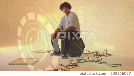 Sitting man wearing light blue sweater on computer towers in studio with cables, HUD graphics Sitting man wearing light blue sweater on computer towers in studio with cables, HUD graphics 139256097