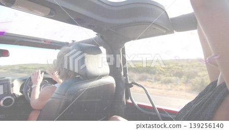 Two friends riding red convertible along rural highway, with steering wheel and dashboard visible Two friends riding red convertible along rural highway, with steering wheel and dashboard visible 139256140