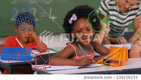 Smiling girl in pink dress writing with pencil in notebook in classroom, with chalkboard equations Smiling girl in pink dress writing with pencil in notebook in classroom, with chalkboard equations 139256233