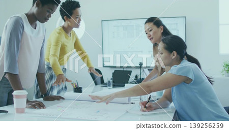 Leaning casually dressed women gesturing and writing at conference table, with blueprints laptop Leaning casually dressed women gesturing and writing at conference table, with blueprints laptop 139256259