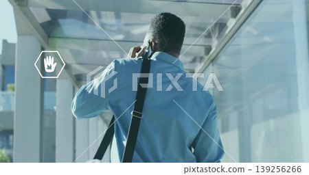 Talking man wearing light blue shirt holding smartphone to ear in glass corridor, messenger bag Talking man wearing light blue shirt holding smartphone to ear in glass corridor, messenger bag 139256266