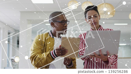 Comparing tablet-holding coworker and laptop-holding peer analyzing data in office, network overlay Comparing tablet-holding coworker and laptop-holding peer analyzing data in office, network overlay 139256286