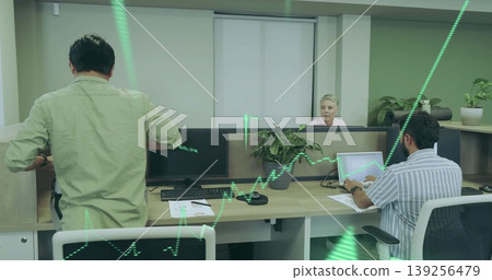 Office colleagues reviewing stock data and typing at laptops in cubicle, with monitors, plants 139256479
