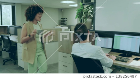 Carrying two coffee mugs, coworker walking past seated colleague in open office, with dual monitors Carrying two coffee mugs, coworker walking past seated colleague in open office, with dual monitors 139256497